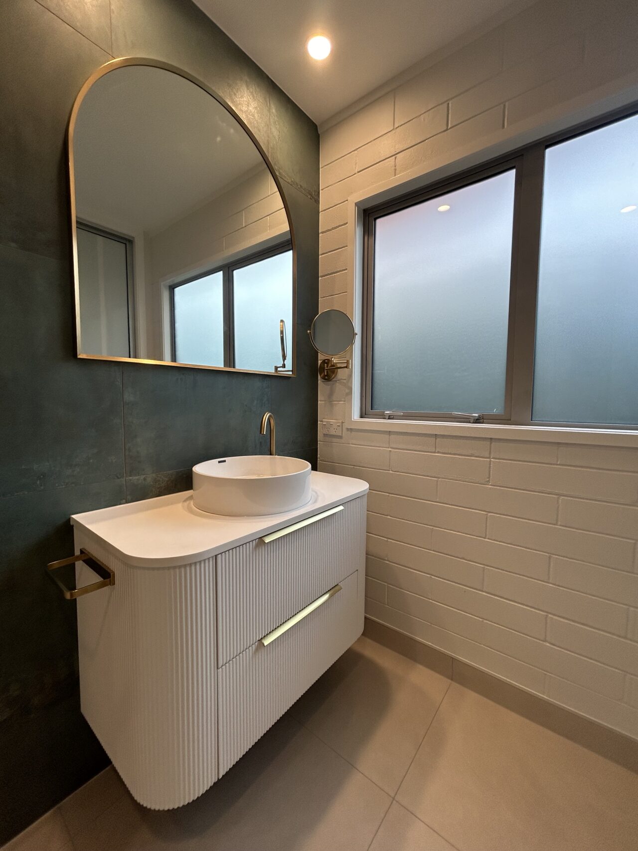 Designer bathroom vanity with round basin, brass tapware, and tiled feature wall
