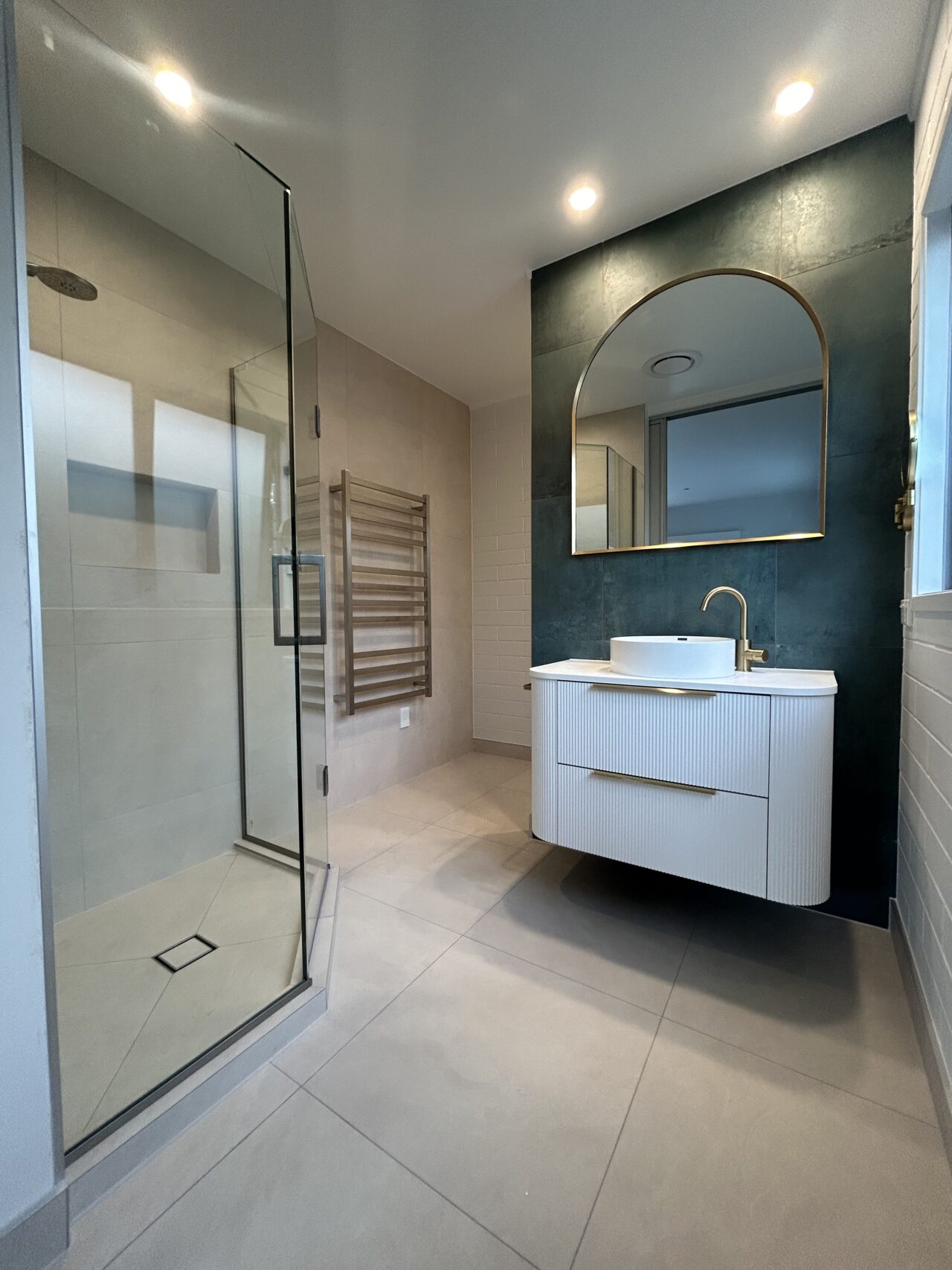 Spacious luxury bathroom with frameless glass shower, brass finishes, and tiled feature wall